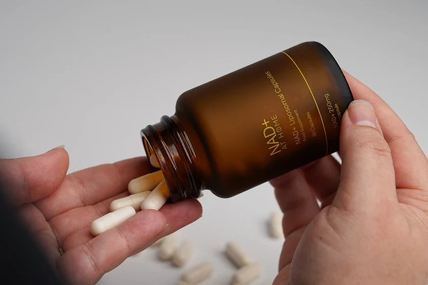 Pouring liposomal NAD+ capsules from an amber supplement bottle into a hand for daily wellness.