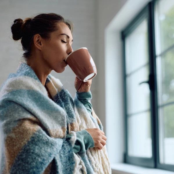 How to Prepare for the Colder Months With NAD+. An image of a woman wrapped in a blanket drinking a mug of tea