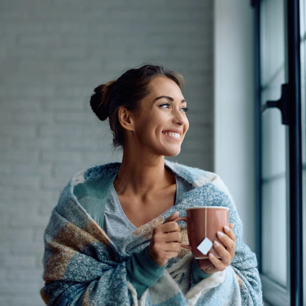 How to Prepare for the Colder Months With NAD+. An image of a woman wrapped in a blanket with a mug of tea