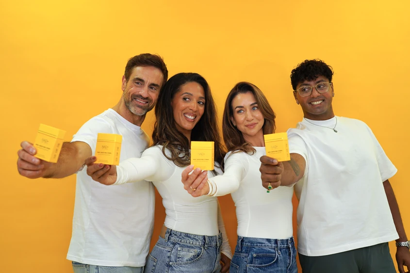 Four smiling friends holding out NAD+ Quick Melt Strips boxes